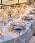 Riviera Blue tablecloth styled on an outdoor banquet table with gold cutlery and candles, golden hour