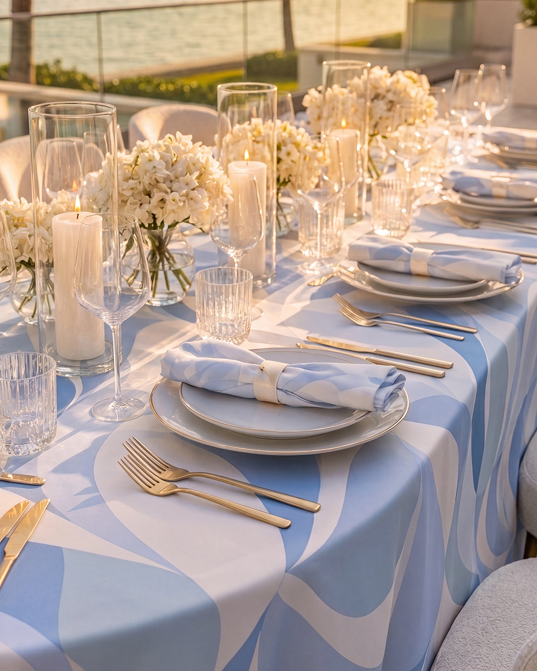 Riviera Blue tablecloth styled on an outdoor banquet table with gold cutlery and candles, golden hour